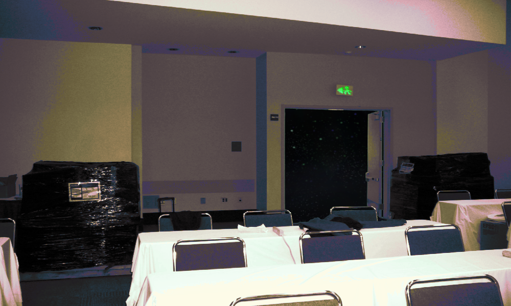 a convention or expo center side room. tables are set up with tableclothes, there is a suitcase in the back, and shipping palettes wrapped in plastic with unknown contents sit in the room. there are at lease two or three rows of tables and three columns. It could  be a panel room. The door leading out of the room opens to an empty tarry and starry black void a convention or expo center side room. tables are set up with tableclothes, there is a suitcase in the back, and shipping palettes wrapped in plastic with unknown contents sit in the room. there are at lease two or three rows of tables and three columns. It could  be a panel room. The door leading out of the room opens to an empty tarry and starry black void